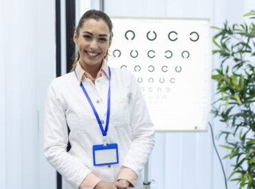 Professional female optician pointing at eye chart, timely diagnosis of vision. Portrait of optician asking patient for an eye exam test with an eye chart monitor at his clinic
